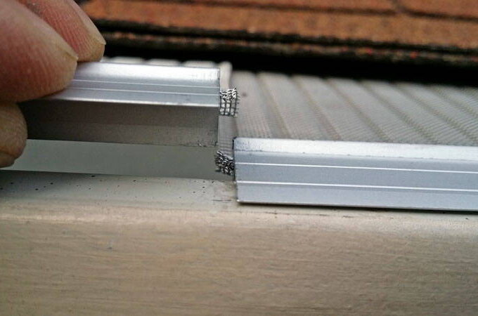 Close-up of fingers holding two metal frame pieces with exposed stainless steel micro-mesh ends, likely for assembling or repairing a window or door screen for easy installation.