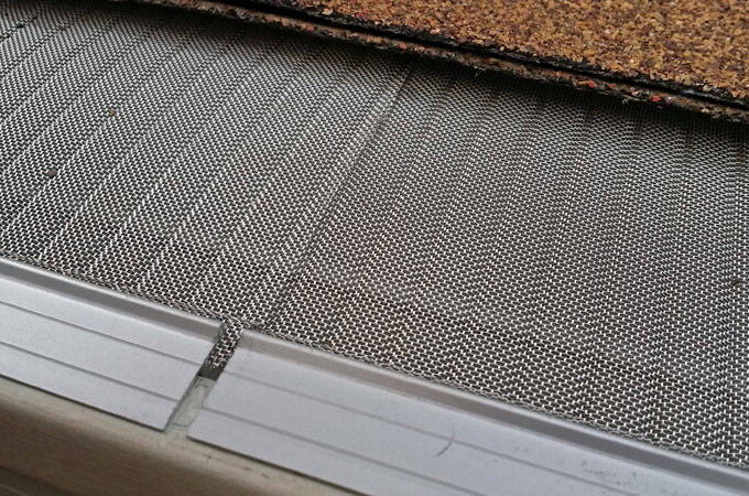 Close-up of a Gutterglove gutter guard with fine mesh installed on a roof edge, partially covered by shingles, designed to prevent debris from entering the gutter. Available at select retailers like Costco.