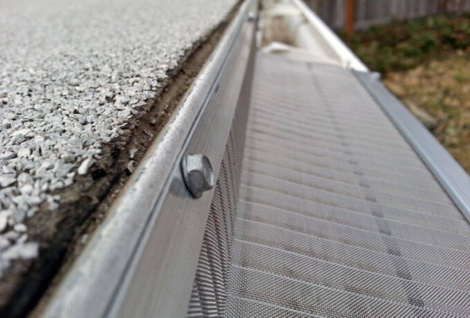 Close-up view of an Easy On Gutter Guard from Costco installed along the edge of a roof with asphalt shingles, featuring a mesh screen that keeps debris out of the gutter.