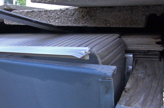 A close-up view of damaged building materials, including bent metal, cracked concrete, and splintered wood—some resembling worn gutter guard and twisted stainless steel micro-mesh—appearing to be crushed together.