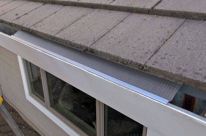 A close-up view of a house roof with gray shingles and a newly installed stainless steel micro-mesh gutter guard over the rain gutter, seen above a set of windows for easy installation.