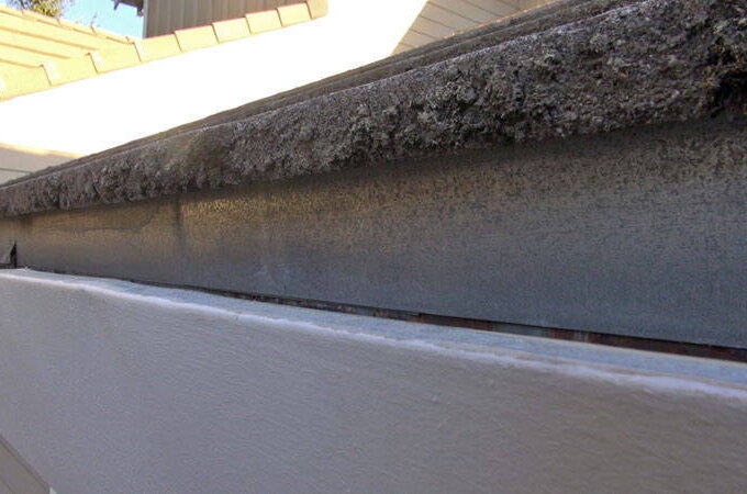 A close-up view of a house’s roof edge shows a gutter filled with dirt and debris, highlighting buildup and the need for cleaning. Installing stainless steel micro-mesh offers easy installation and helps prevent future clogs.