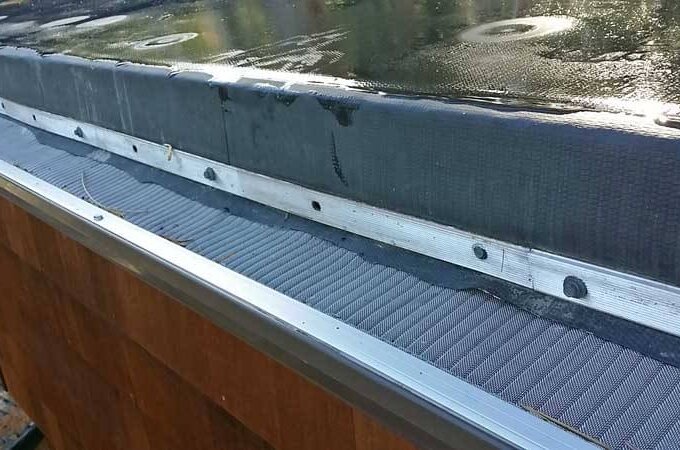 Close-up of a roof edge with a Gutterglove mesh gutter guard installed, showing its cover designed to prevent debris from entering the gutter. The roof above appears to be wet.