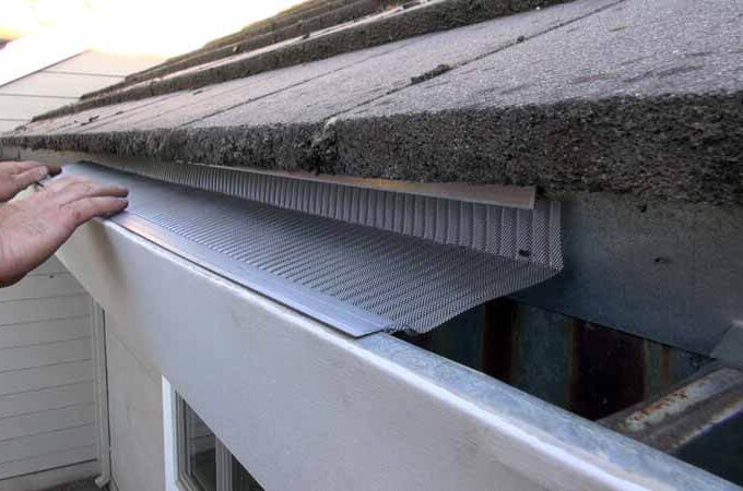 A person installs a Gutterglove metal gutter guard along the edge of a roof for easy installation and to prevent debris from entering the gutter system.