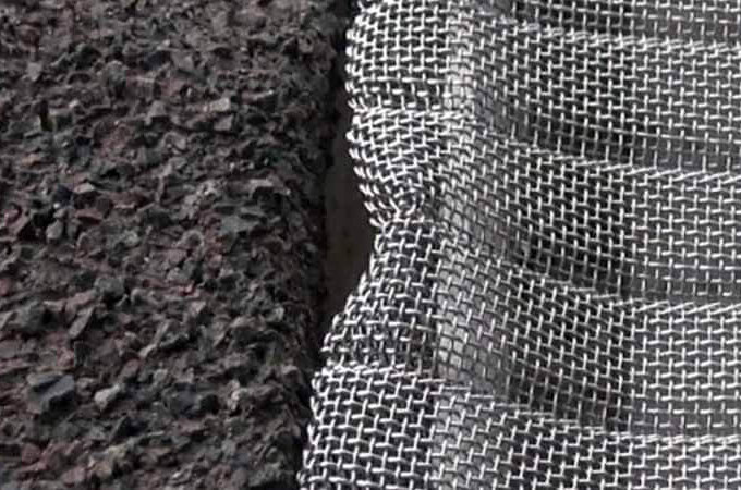 Close-up of a textured black surface next to a wavy, woven metal mesh, showing the contrast between rocky material and shiny grid—perfect for demonstrating the durability and easy installation of Easy On Gutter Guard.