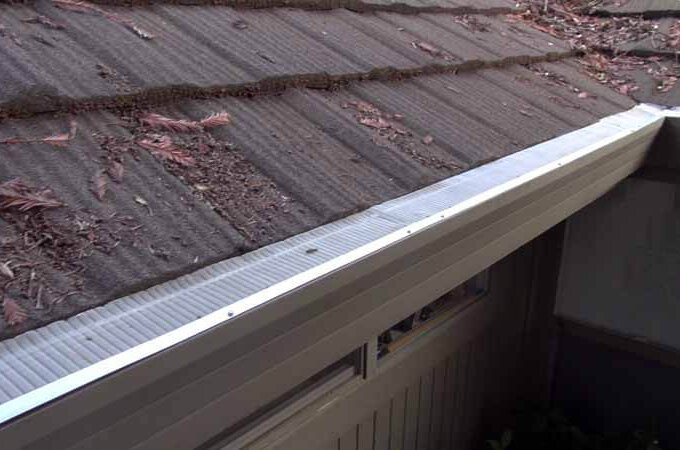 A roof with a brown metal gutter guard installed for easy installation, preventing leaves and debris from entering the gutter; dry leaves and twigs are scattered on the roof.