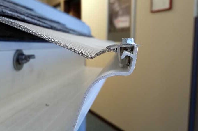 Close-up of a white metal or plastic track with an attached mesh or fabric screen, possibly part of a window or door frame, in an indoor setting.