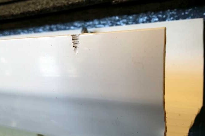 Close-up of a white piece of wood or trim with three small cracks or splits near the edge, possibly caused by a screw or nail that has damaged the surface.