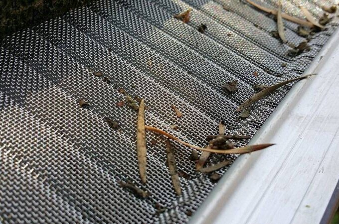 Close-up of an Easy On Gutter Guard with small debris, dirt, and a few dry leaves scattered on top, effectively blocking large debris from entering the gutter below.